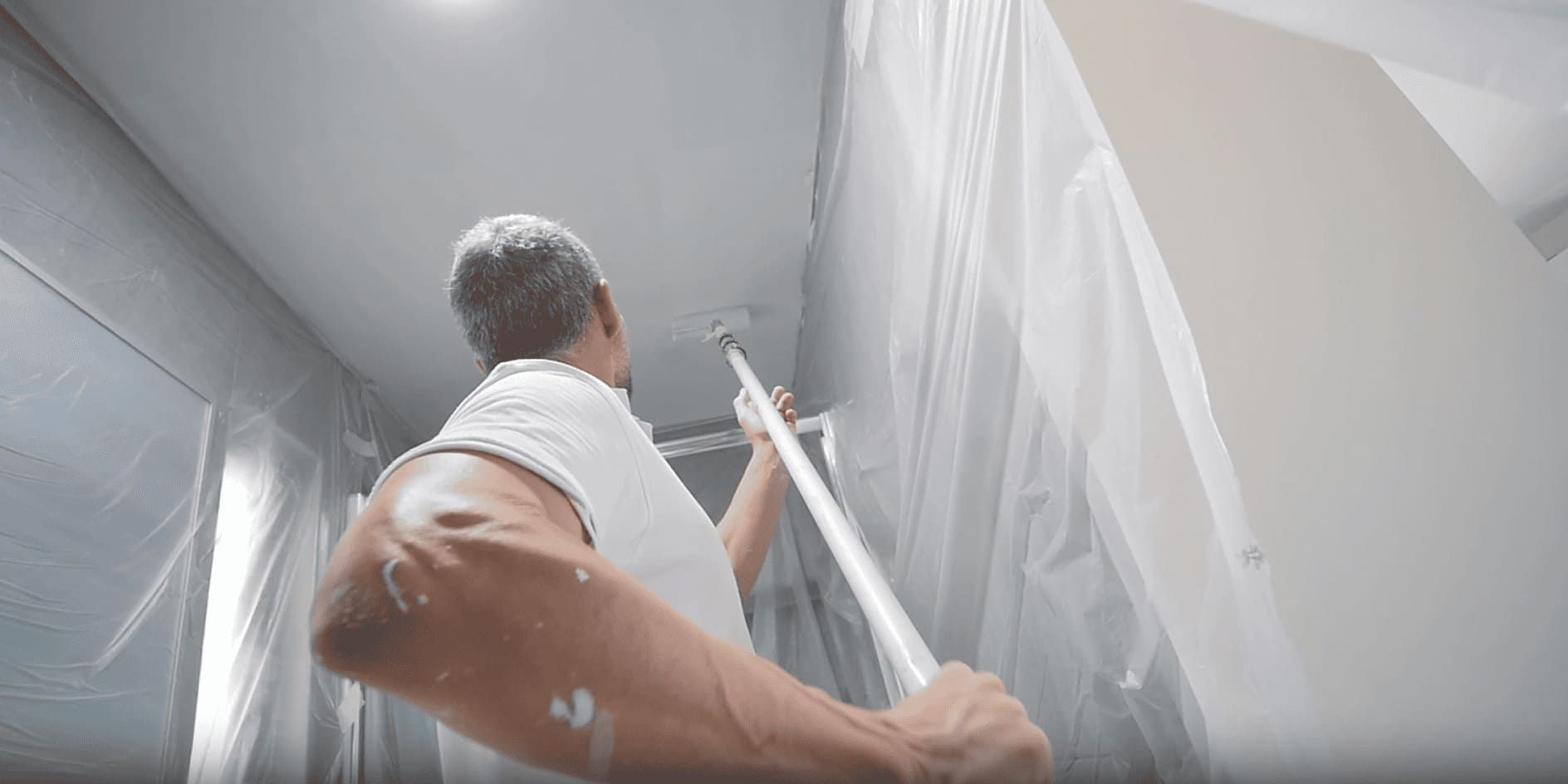 Ein Maler streicht mit einer Teleskoprolle eine Zimmerdecke